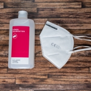 Auf einem braunen Holztisch liegt eine FFP2 Maske und eine Desinfektionmittelflasche. Desinfektionsmittel und eine FFP2 Maske zum Schutz gegen den Virus Covis-19.